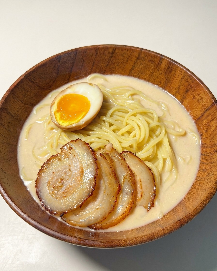 Un cuenco de ramen coronado con cerdo y medio huevo pasado por agua con una yema naranja brillante.