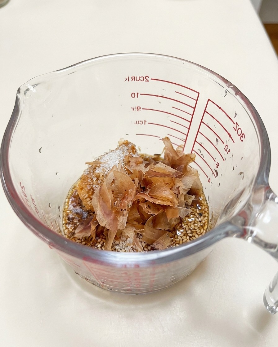 Copos de bonito colocados sobre la pasta de miso y las semillas de sésamo en una jarra medidora.
