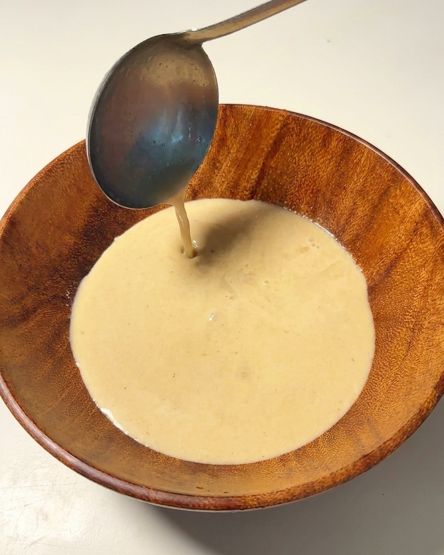 Caldo de cerdo cremoso y caliente vertiéndose desde un cazo a un cuenco de madera.