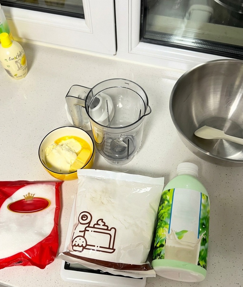 Ingredientes de repostería sobre la encimera, incluyendo una botella de leche, azúcar, harina, mantequilla y queso crema.