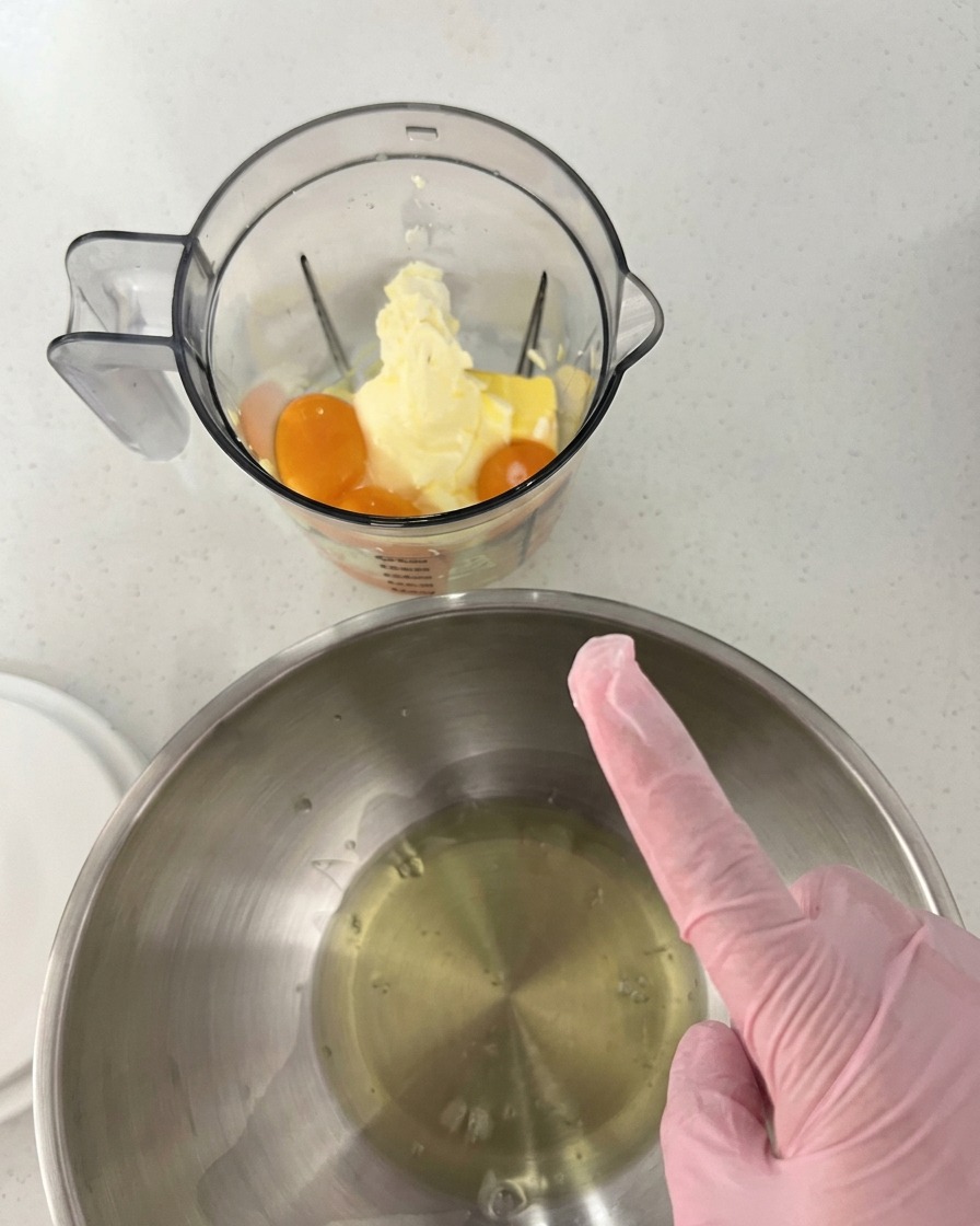 Yemas de huevo, mantequilla y queso crema en el vaso de la licuadora, junto a un bol de acero inoxidable con claras de huevo.