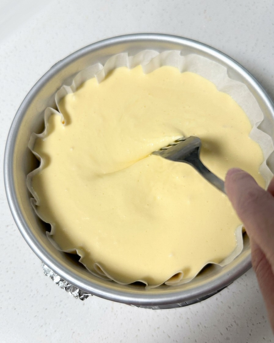 Una mano usando un tenedor para trazar espirales suavemente en la superficie de la masa dentro del molde forrado.