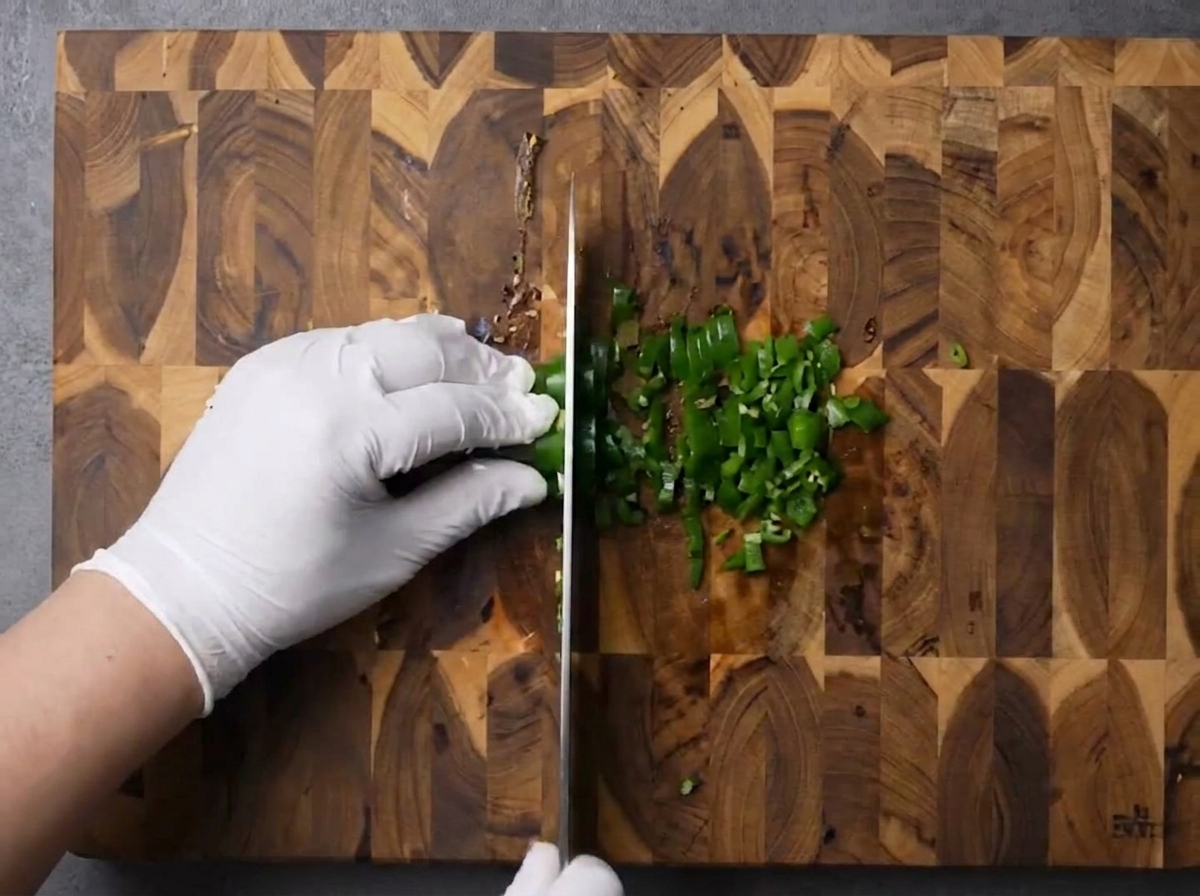 Manos picando finamente chiles verdes sobre una tabla de cortar.