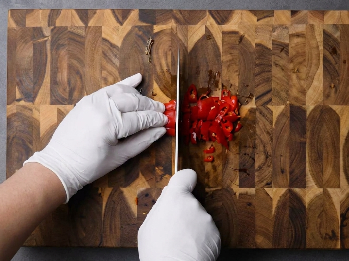 Manos picando finamente chiles rojos frescos sobre una tabla de madera.
