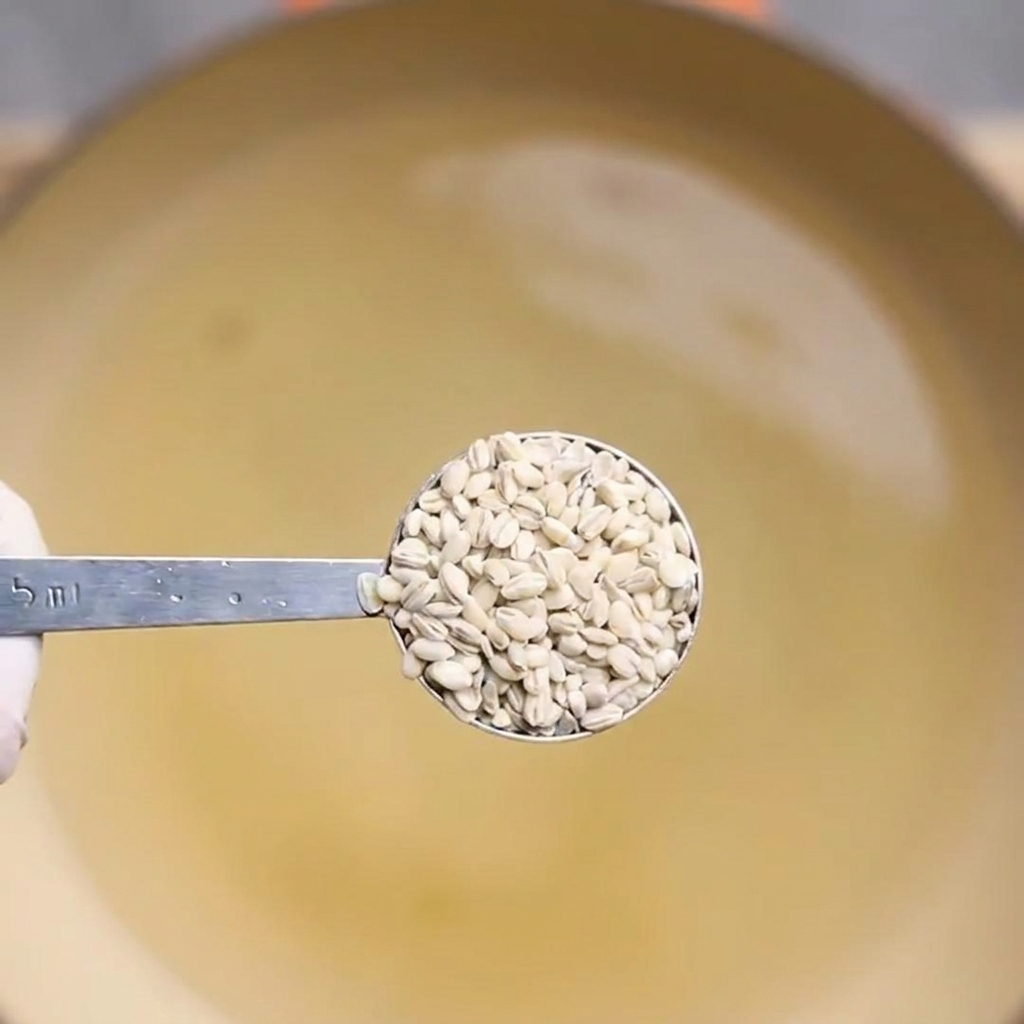 Una cuchara sacando cebada cocida de una olla con agua hirviendo.