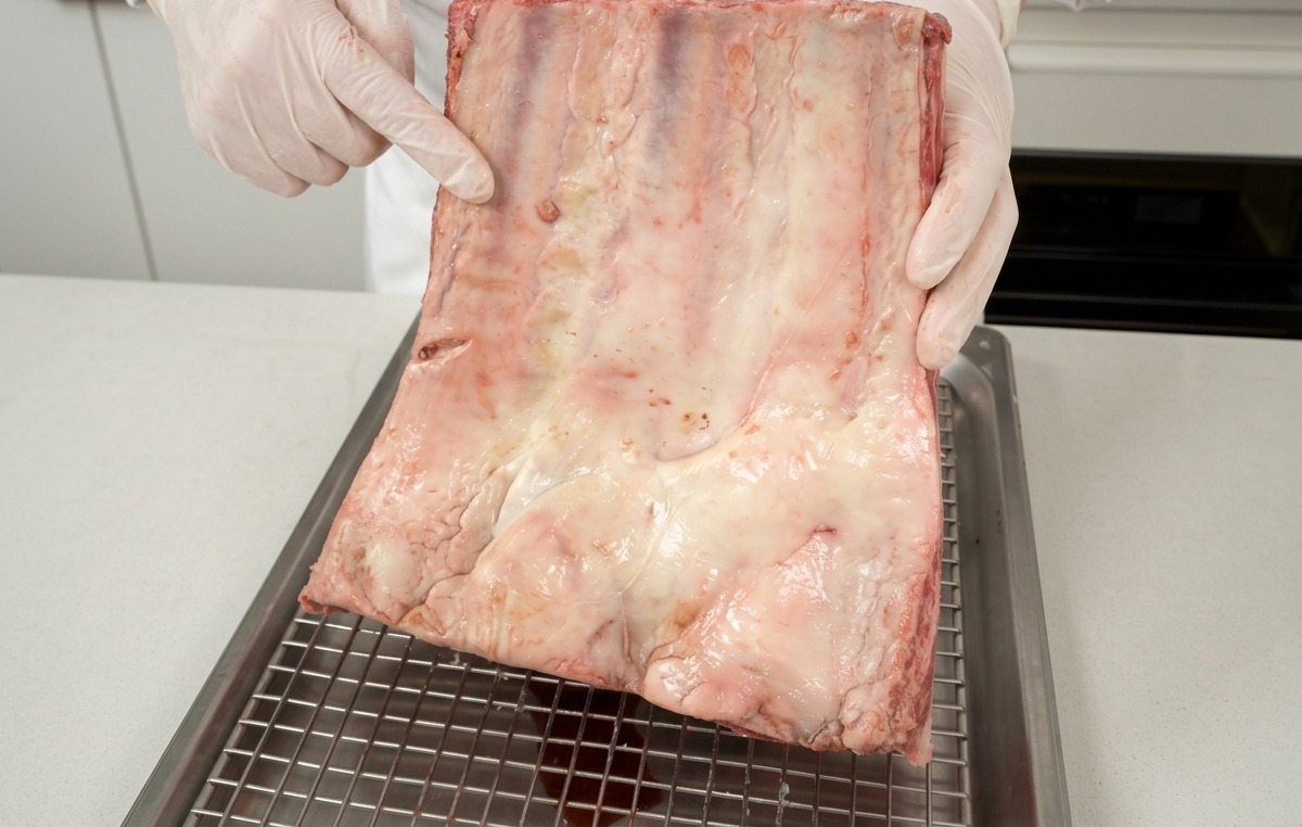 Un chef sosteniendo un costillar de ternera crudo, mostrando el veteado de grasa blanca.
