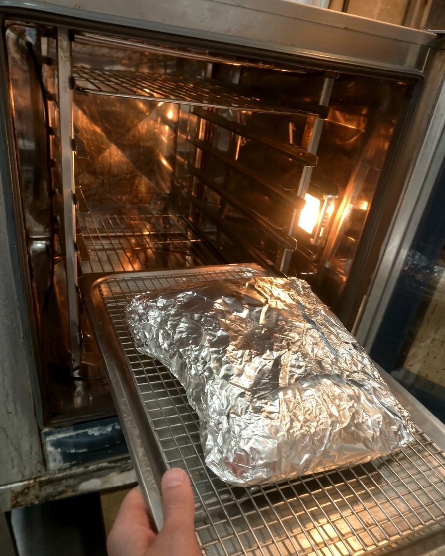 El paquete de costillas envuelto en aluminio sobre una rejilla entrando al horno caliente.