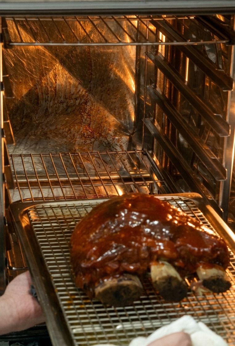 Manos metiendo la bandeja con las costillas glaseadas en el horno a alta temperatura.