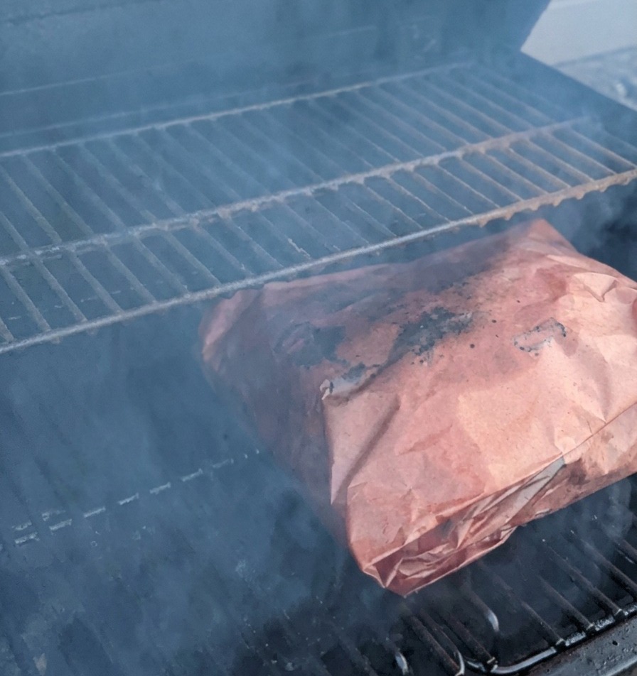 Costillas envueltas en papel de carnicero cocinándose en el ahumador rodeadas de humo.
