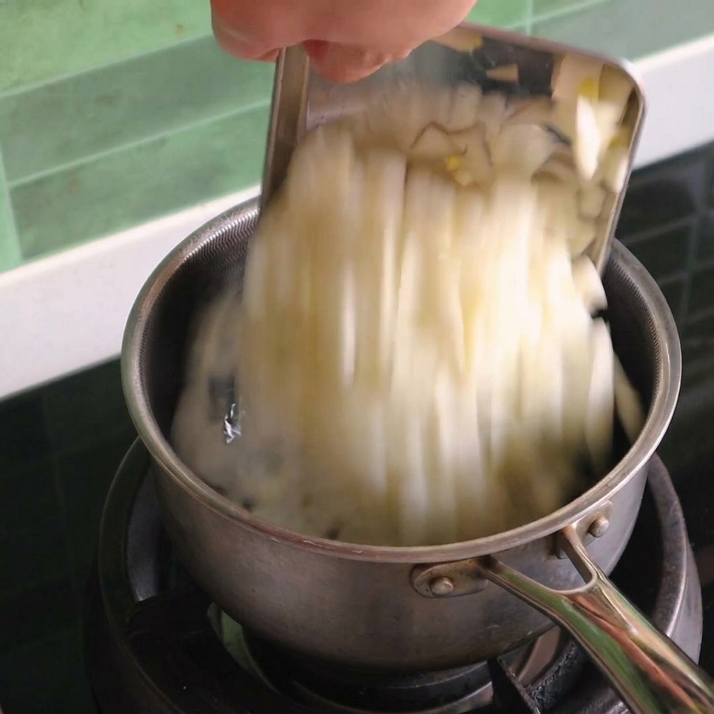 Cebolla blanca picada cayendo desde un raspador de metal a una olla de acero inoxidable en una estufa de gas.