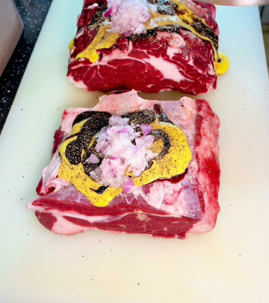 Carne cruda cubierta con salsas y cebolla morada picada sobre una tabla de cortar.
