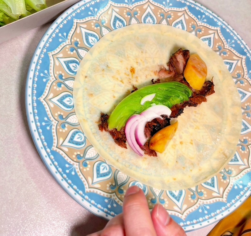 Carne ahumada picada con aguacate y cebolla roja en el centro de una tortilla en un plato decorativo.