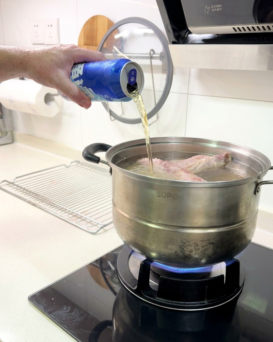 Cerveza vertiéndose desde una lata de aluminio azul en una olla con costillas hirviendo en una estufa de gas.