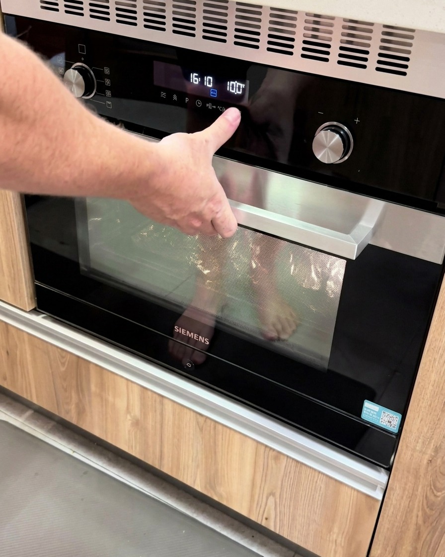 Una mano presionando un botón en un panel digital de un horno moderno configurado a 100 grados.