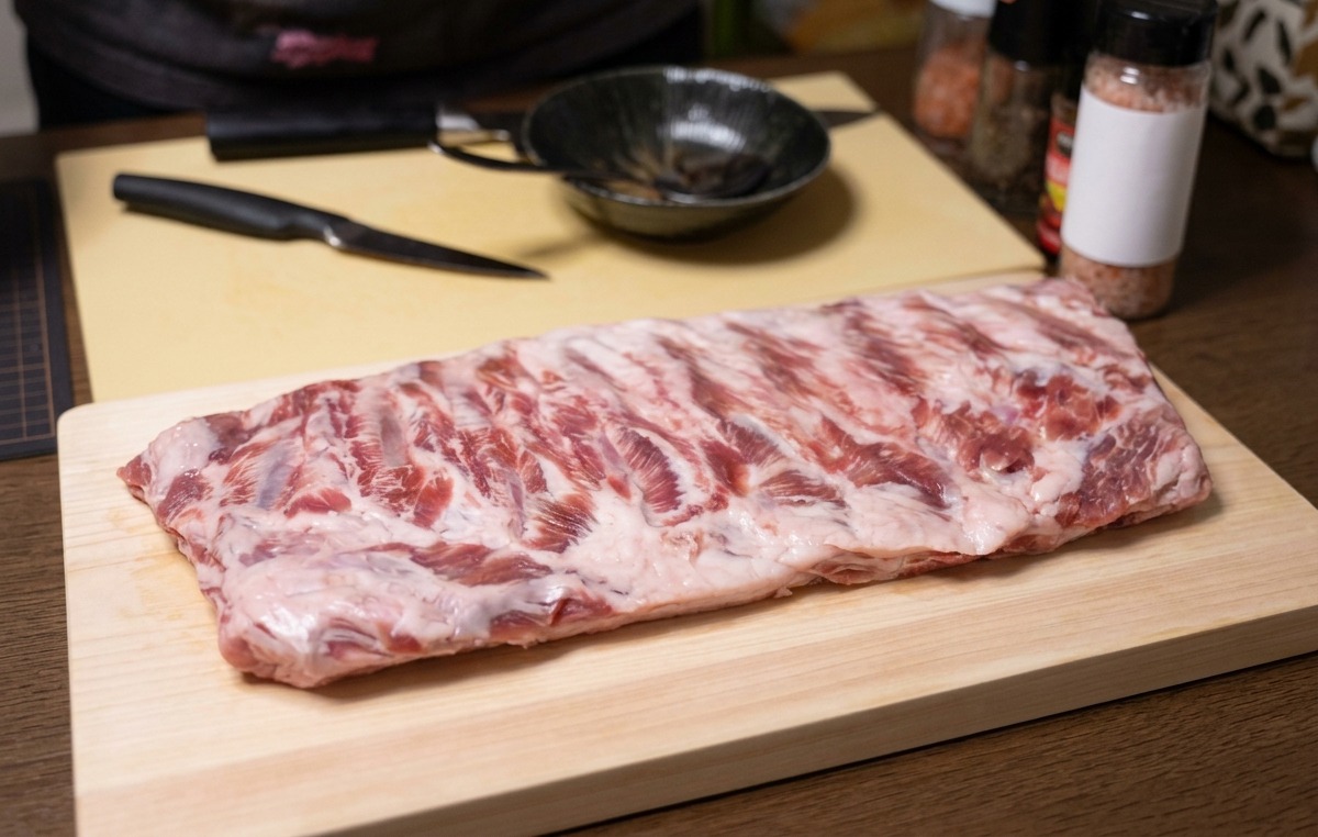 Un costillar de cerdo crudo sobre una tabla de cortar de madera con un cuchillo al lado.