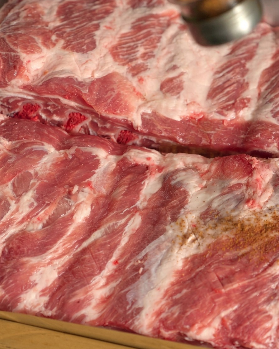 Especias secas siendo espolvoreadas sobre la superficie de las costillas de cerdo crudas.