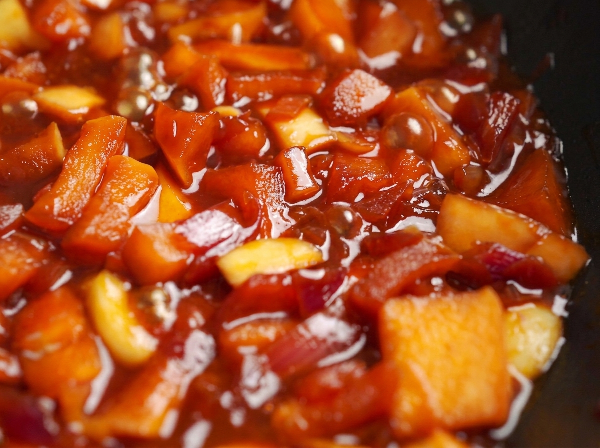 Manzanas y cebollas picadas hirviendo a fuego lento en una rica salsa roja en una sartén.