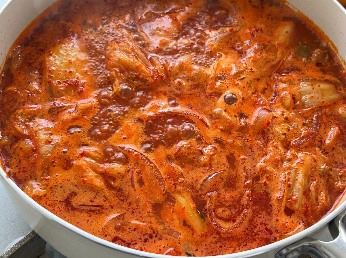 Primer plano de una sopa de kimchi rojo brillante hirviendo vigorosamente en una sartén.