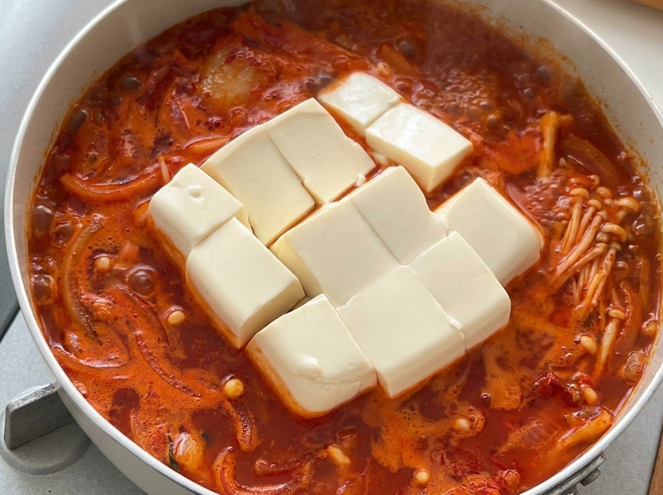 Grandes dados de tofu blanco y suave reposando en un estofado coreano de kimchi caliente y burbujeante.