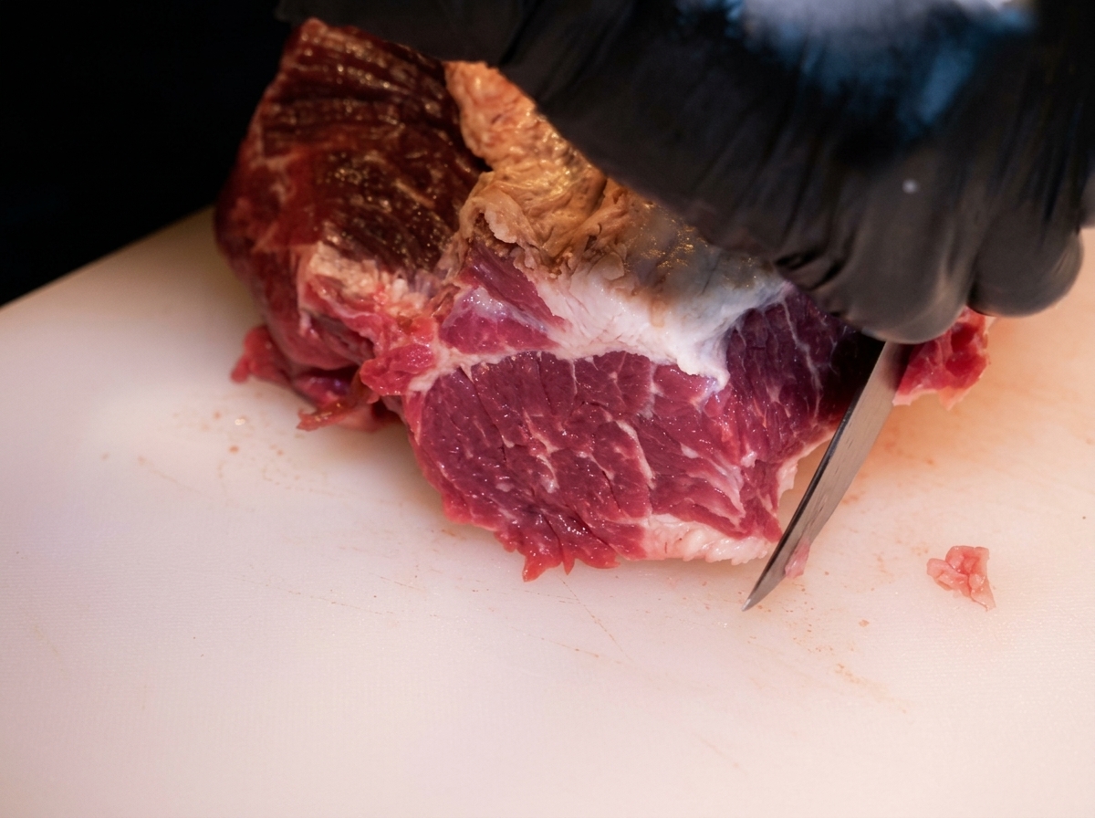 Primer plano de manos con guantes usando un cuchillo para quitar el exceso de grasa de un brisket de res crudo