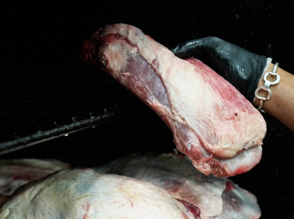 Mano con guante negro colocando un corte grande de carne cruda sobre las rejillas de un ahumador negro