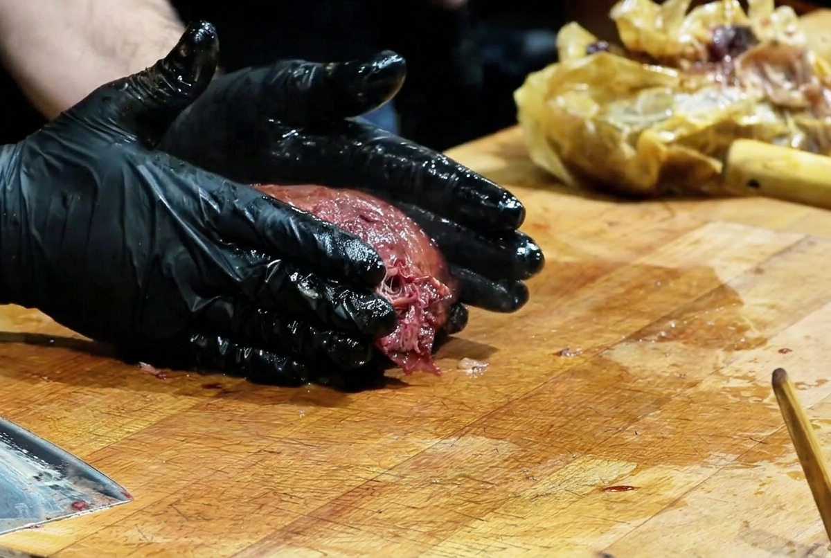 Chef con guantes presionando un brisket ahumado oscuro sobre una tabla para deshebrar la carne
