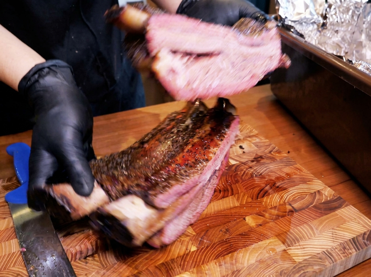Un costillar grande de res ahumada con una costra oscura mostrando un interior jugoso y rosado