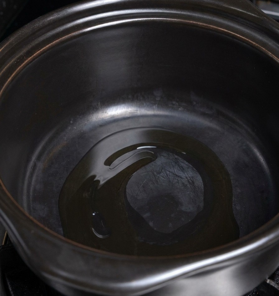 Una fina capa de aceite de cocina brillando en el fondo de una olla de cerámica oscura y caliente.