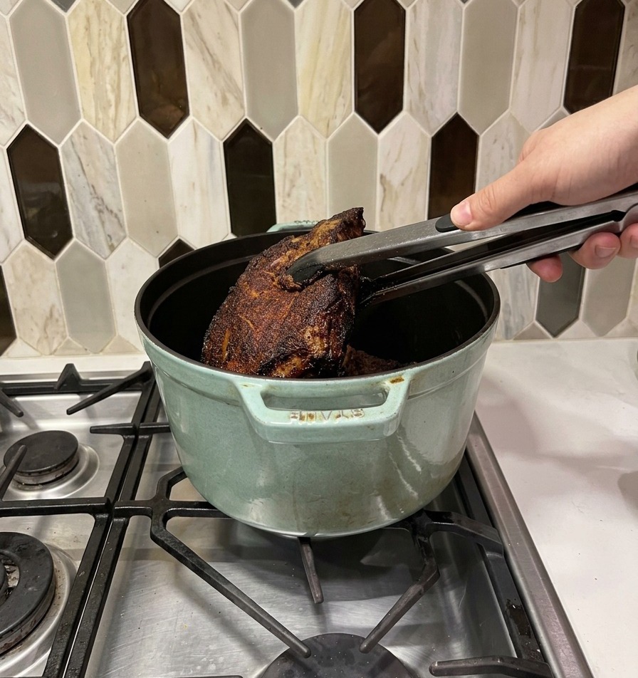 Trozos de carne bien sellados siendo trasladados con pinzas de metal a una olla holandesa de color verde claro.