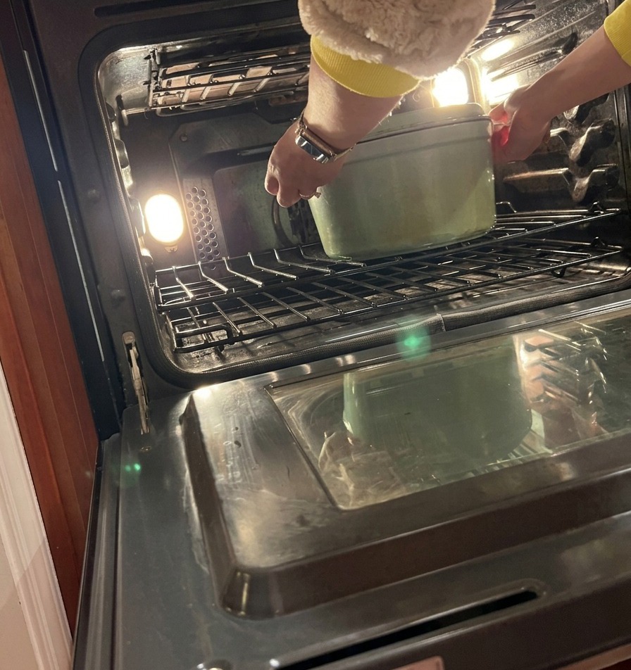 Una persona colocando con cuidado una olla holandesa tapada en la rejilla central de un horno precalentado.