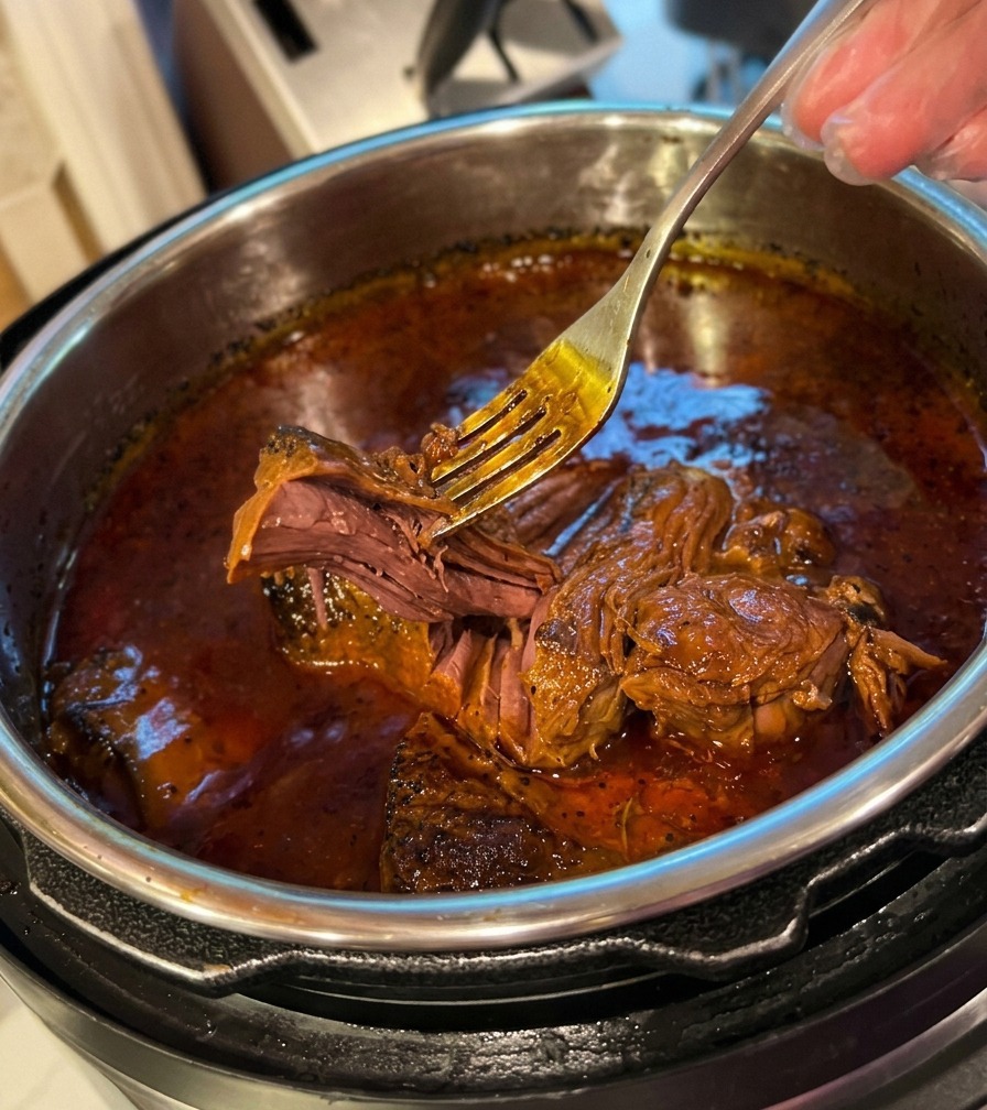 Un tenedor de metal desmechando sin esfuerzo carne muy tierna en una salsa oscura dentro de una olla.