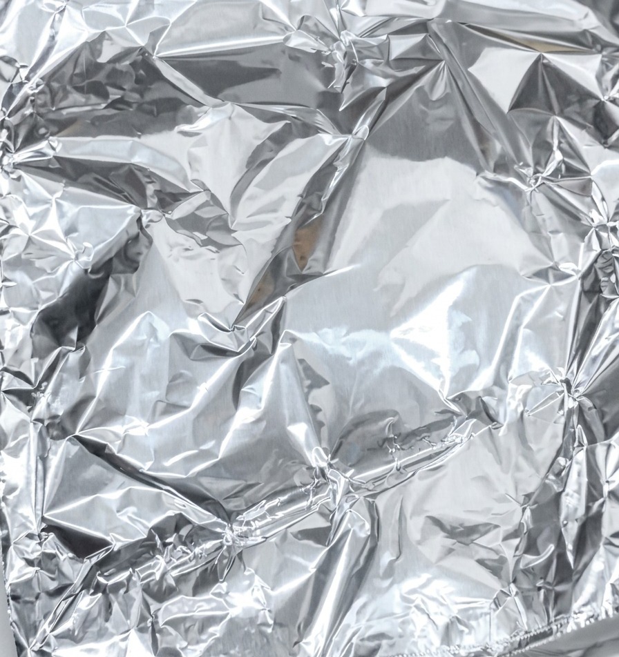 Primer plano de papel de aluminio brillante siendo doblado y sellado para envolver un trozo de cerdo marinado.