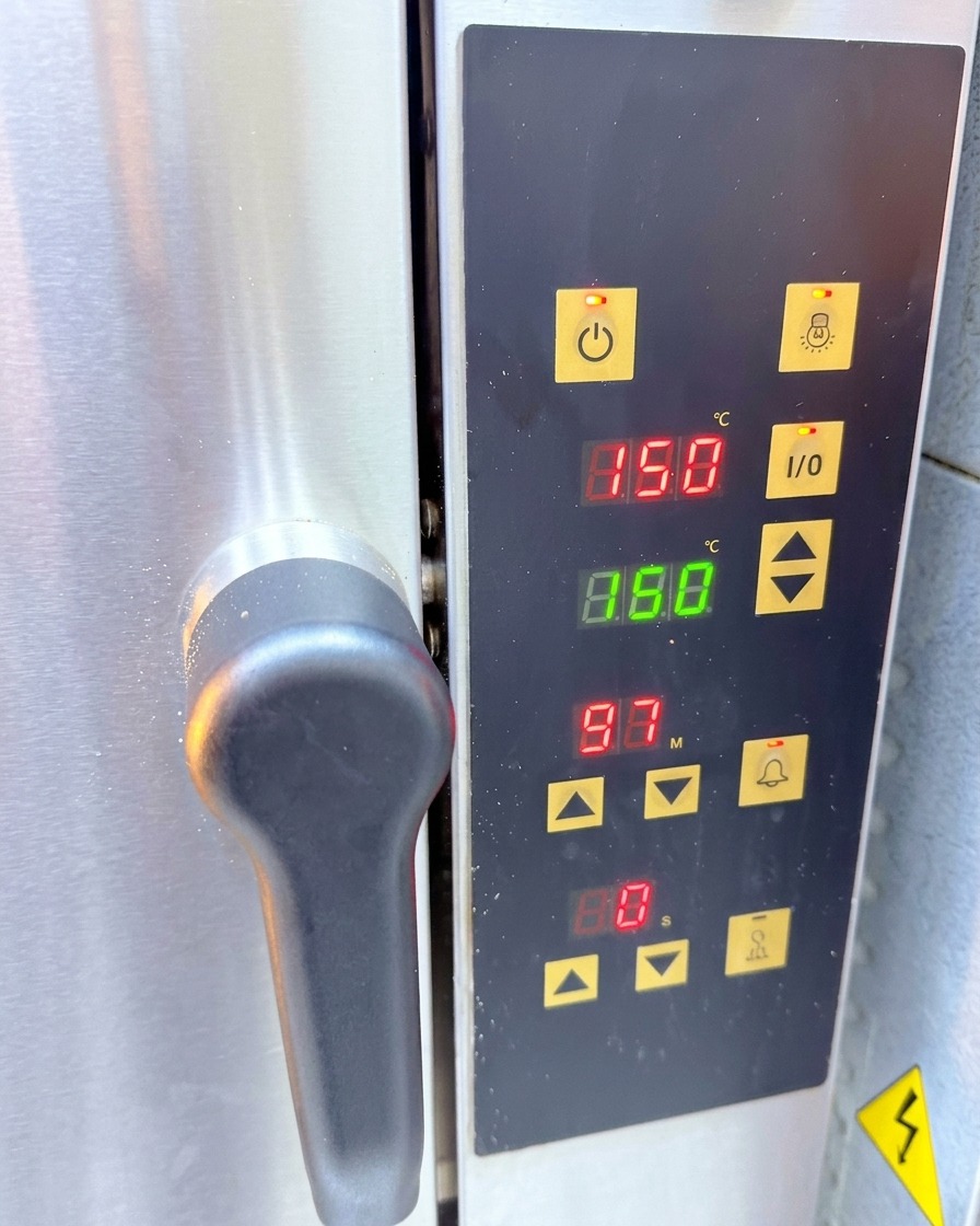 Panel de control de un horno de convección de acero inoxidable mostrando una lectura digital de 150 grados centígrados.