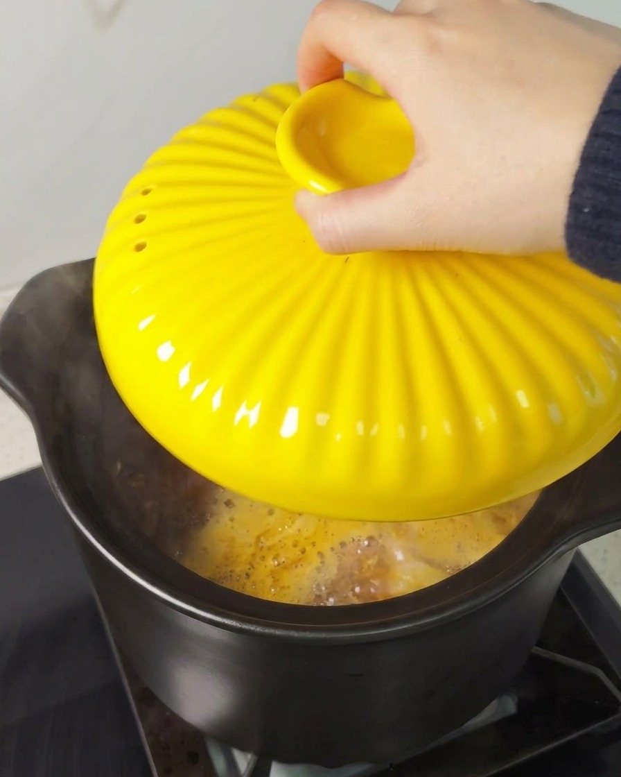 Una mano colocando una tapa amarilla brillante sobre una olla negra en la estufa.