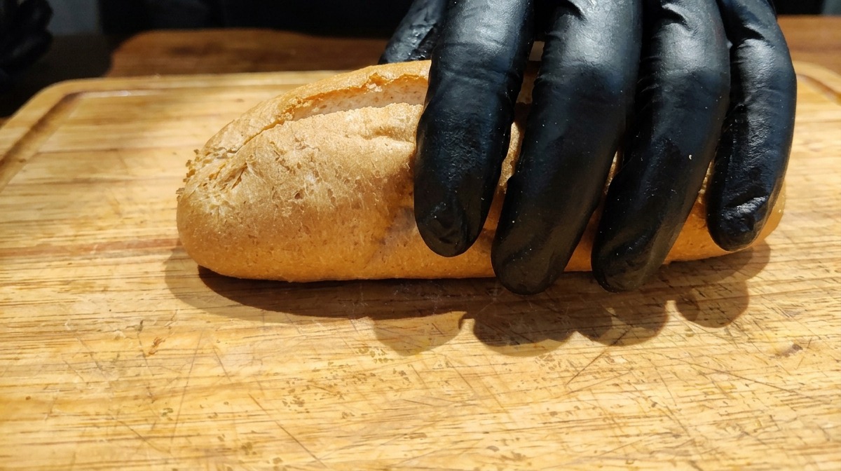 Mano colocando una baguette de trigo integral abierta longitudinalmente sobre una tabla de madera.