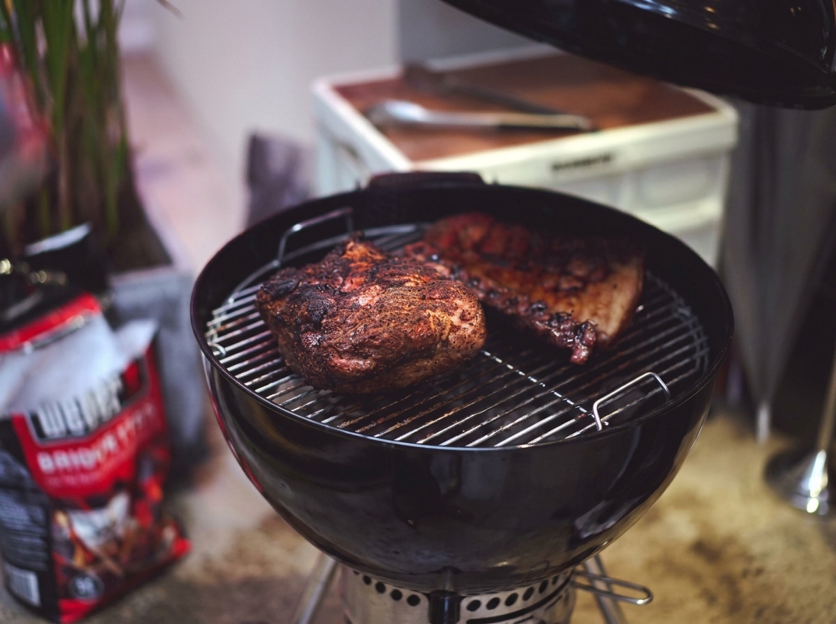 Paleta de cerdo y costillas a medio cocinar con una costra oscura caramelizada sobre la rejilla.