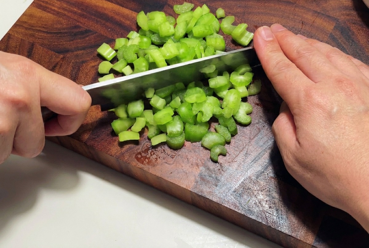 Cebolla blanca siendo picada finamente en cubos sobre una tabla de madera oscura.