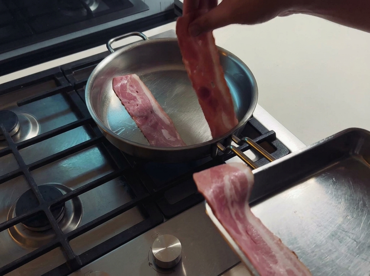 Tiras de tocino friéndose en una sartén de acero inoxidable mientras sueltan su grasa natural.