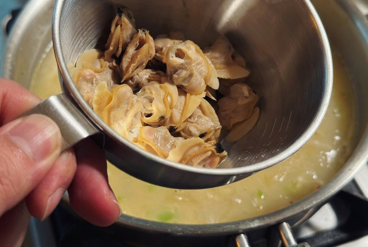 Crema de leche vertiéndose en la sopa espesa mientras se incorpora suavemente la carne de las almejas.