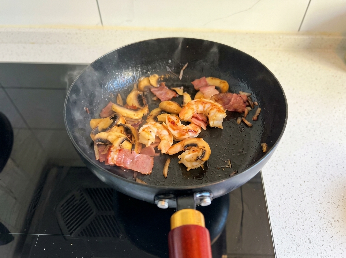 Salteando camarones, tocino y champiñones en una sartén negra hasta que los camarones estén rosados.