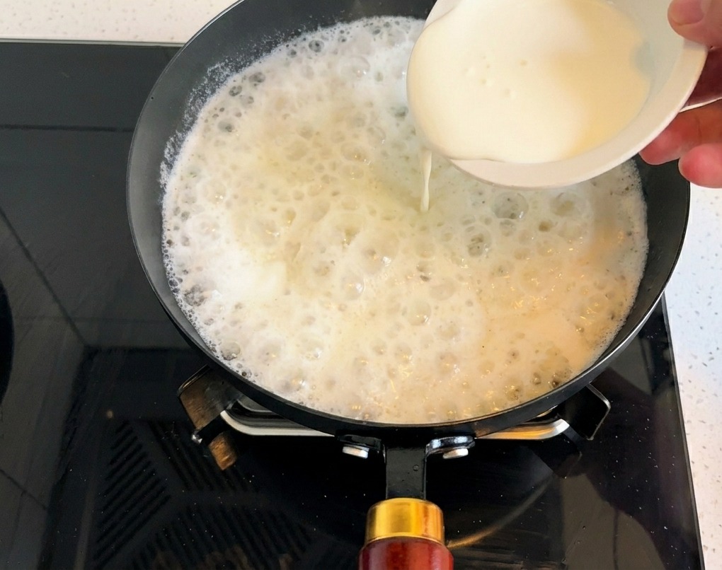 Crema de leche espesa vertiéndose en la base blanquecina de la sopa.