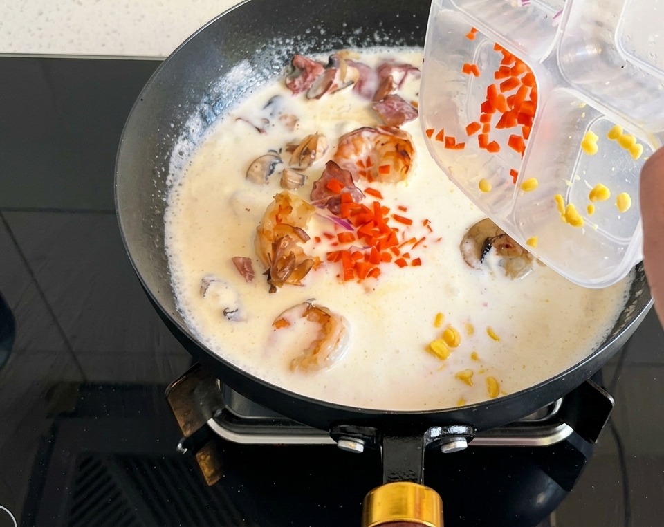 Zanahoria picada y maíz dulce cayendo en la crema de champiñones burbujeante.