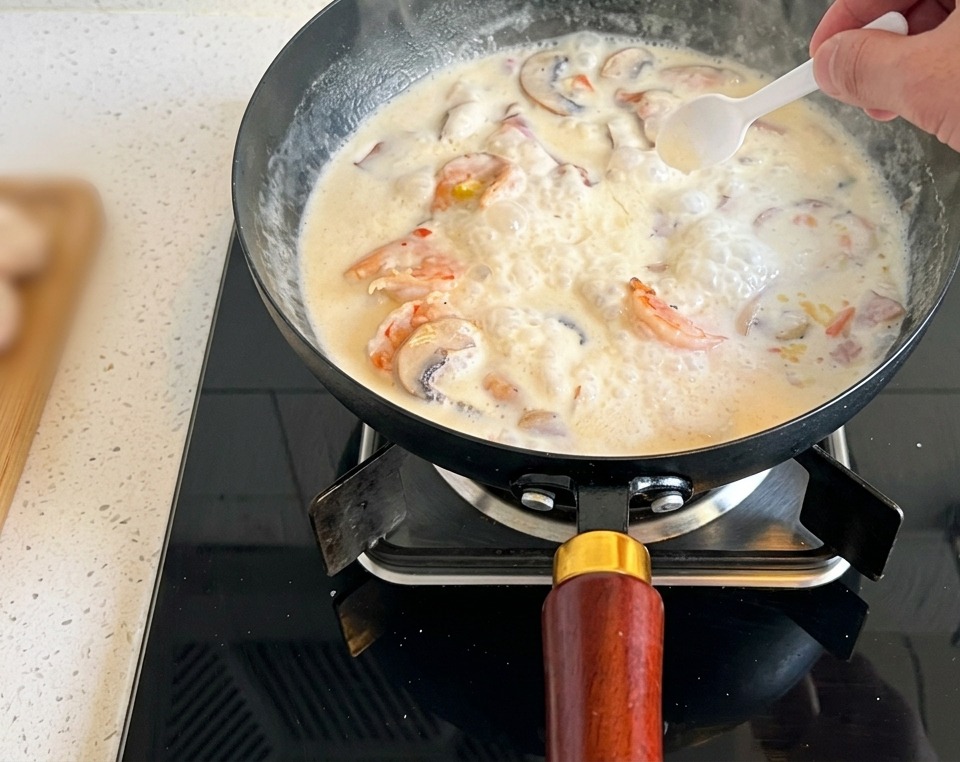 Una cuchara pequeña añadiendo una pizca de sal a la crema de champiñones.