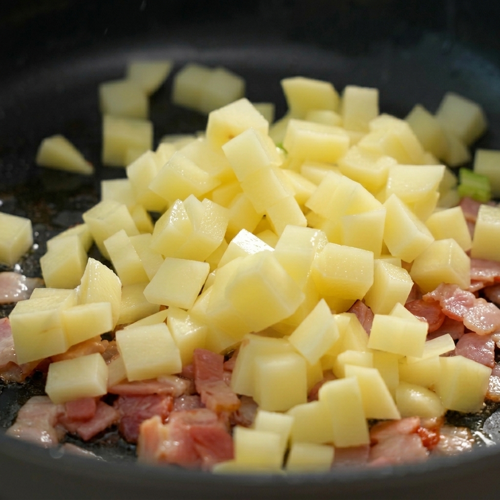 Patatas picadas cayendo en una sartén sobre el beicon troceado.
