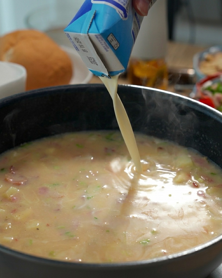 Nata líquida vertiéndose desde un brick en una sartén con la base del clam chowder hirviendo.