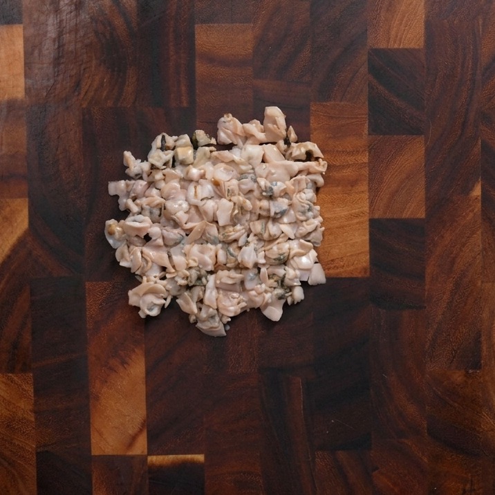 Carne de almeja picada de forma tosca en el centro de una tabla de madera.
