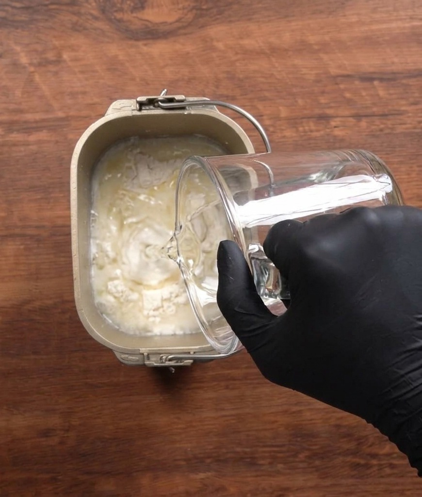 Vertiendo agua en el molde de una panificadora con harina y otros ingredientes.