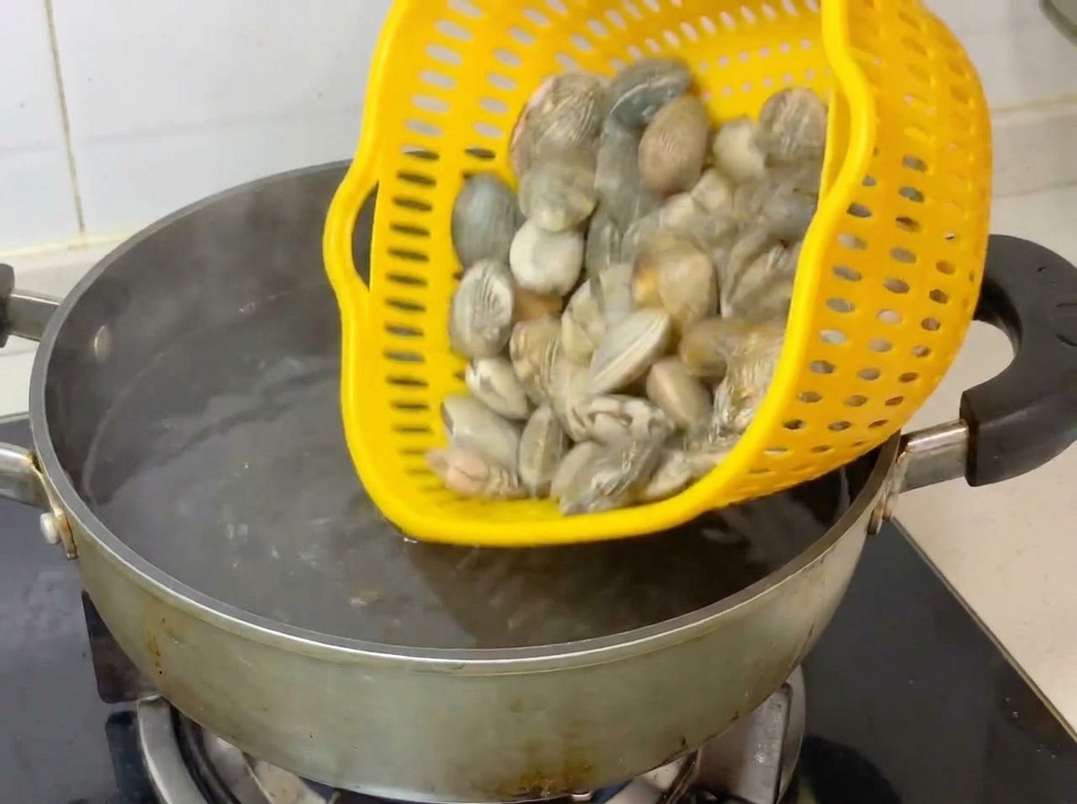 Almejas frescas vertiéndose desde un colador amarillo en una olla con agua hirviendo.
