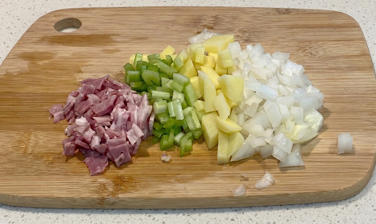 Montones de bacon, apio, patatas y cebollas picadas dispuestos sobre una tabla de cortar de madera.