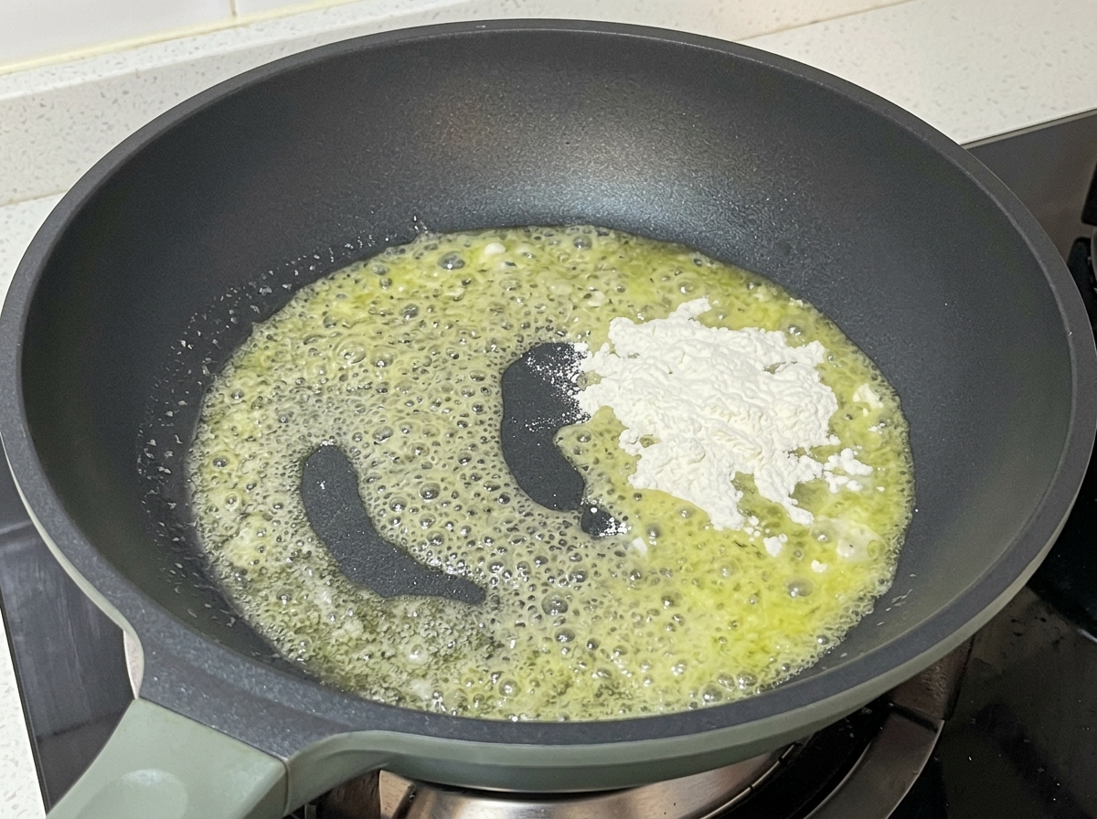 Sartén con mantequilla burbujeante y una montaña de harina blanca siendo mezclada.